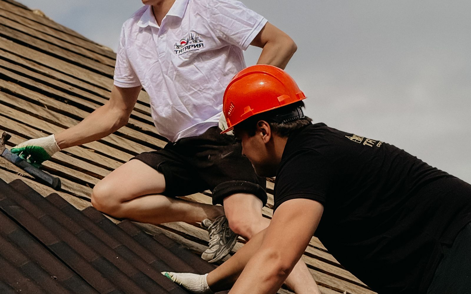 Two roofers in hard hats working together on a sloped roof