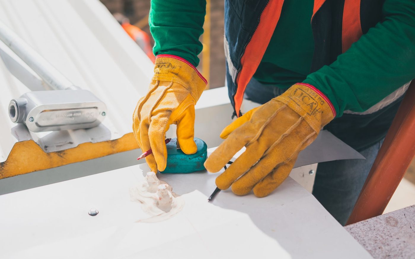 Gloved hands cutting a white roofing sheet with a knife