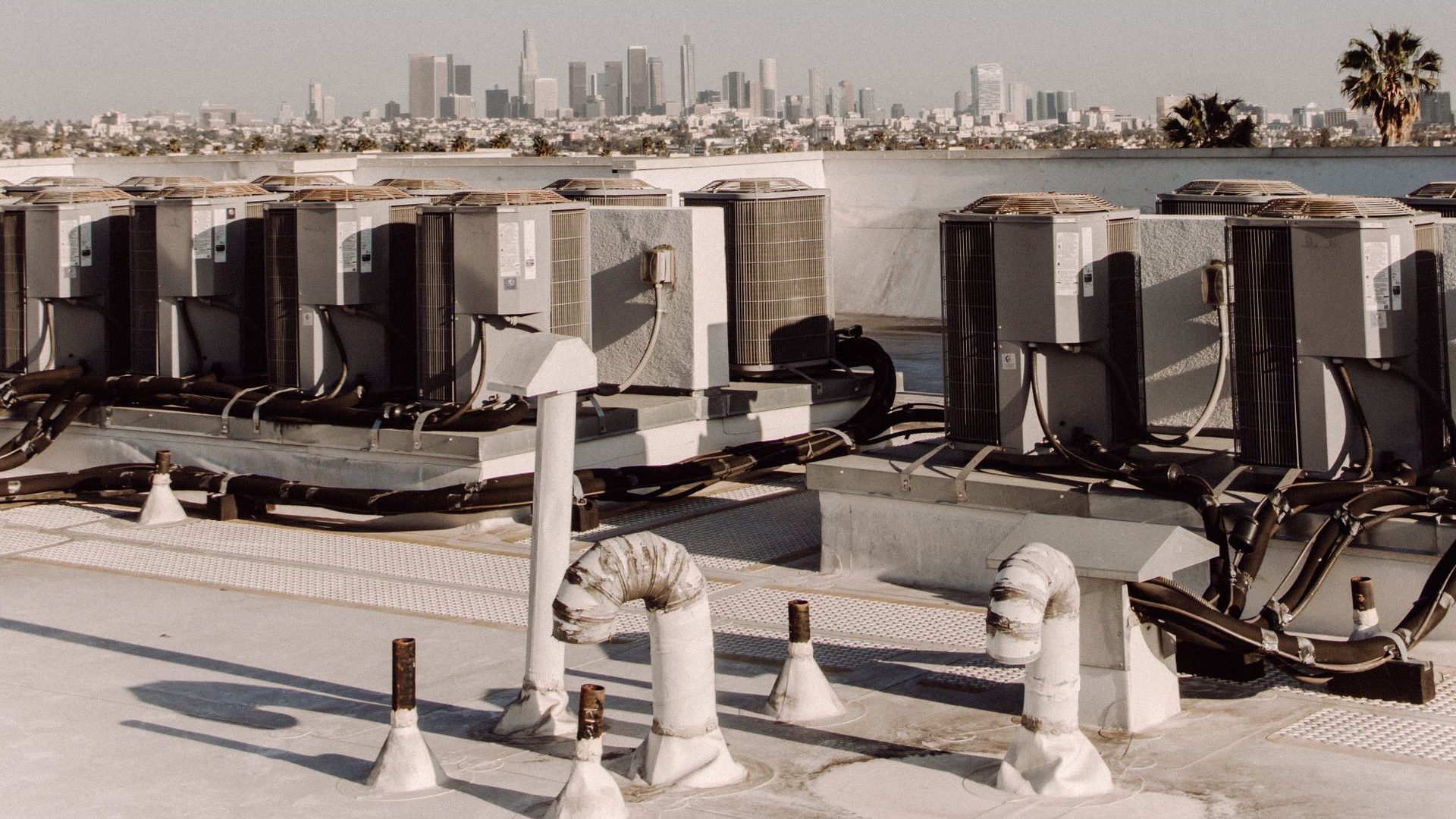 Rooftop units and pipework on a white roof, a city skyline behind