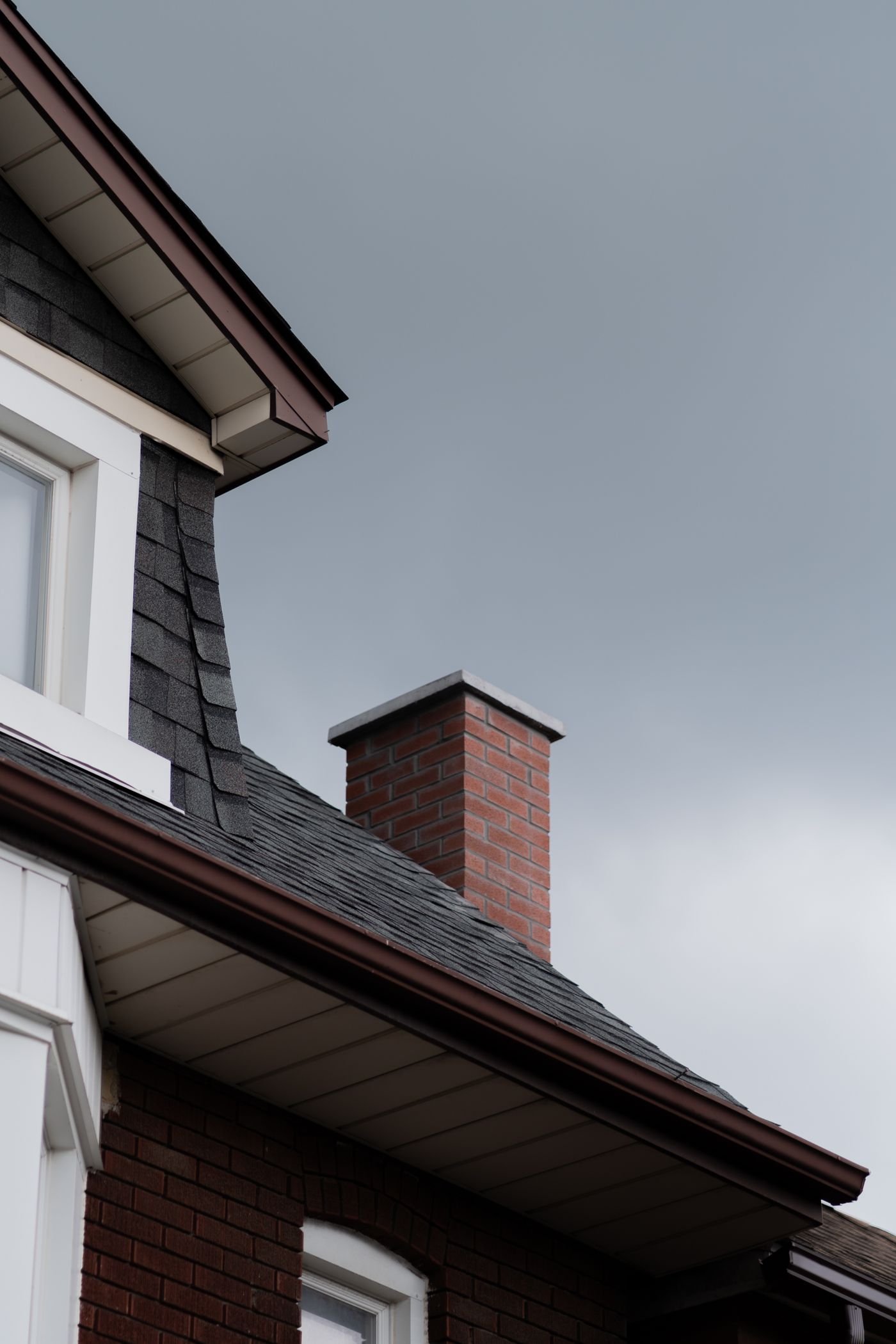 Brick chimney rising through a dark gray shingle roof beside a white gable