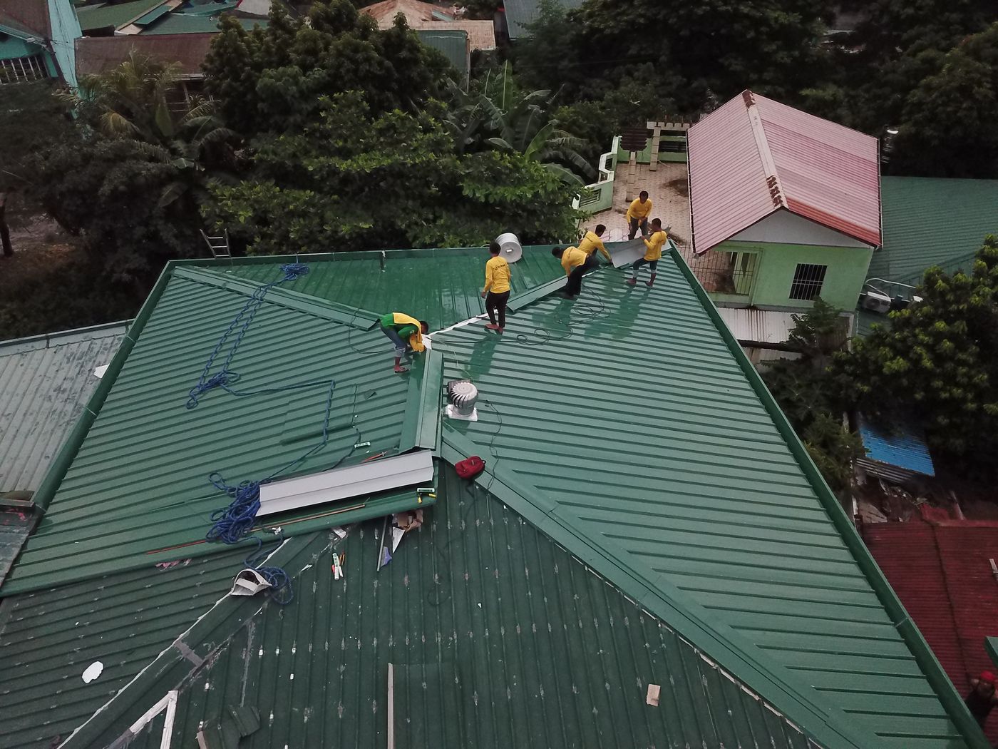Aerial view of a roofing crew in yellow shirts working on a green metal roof