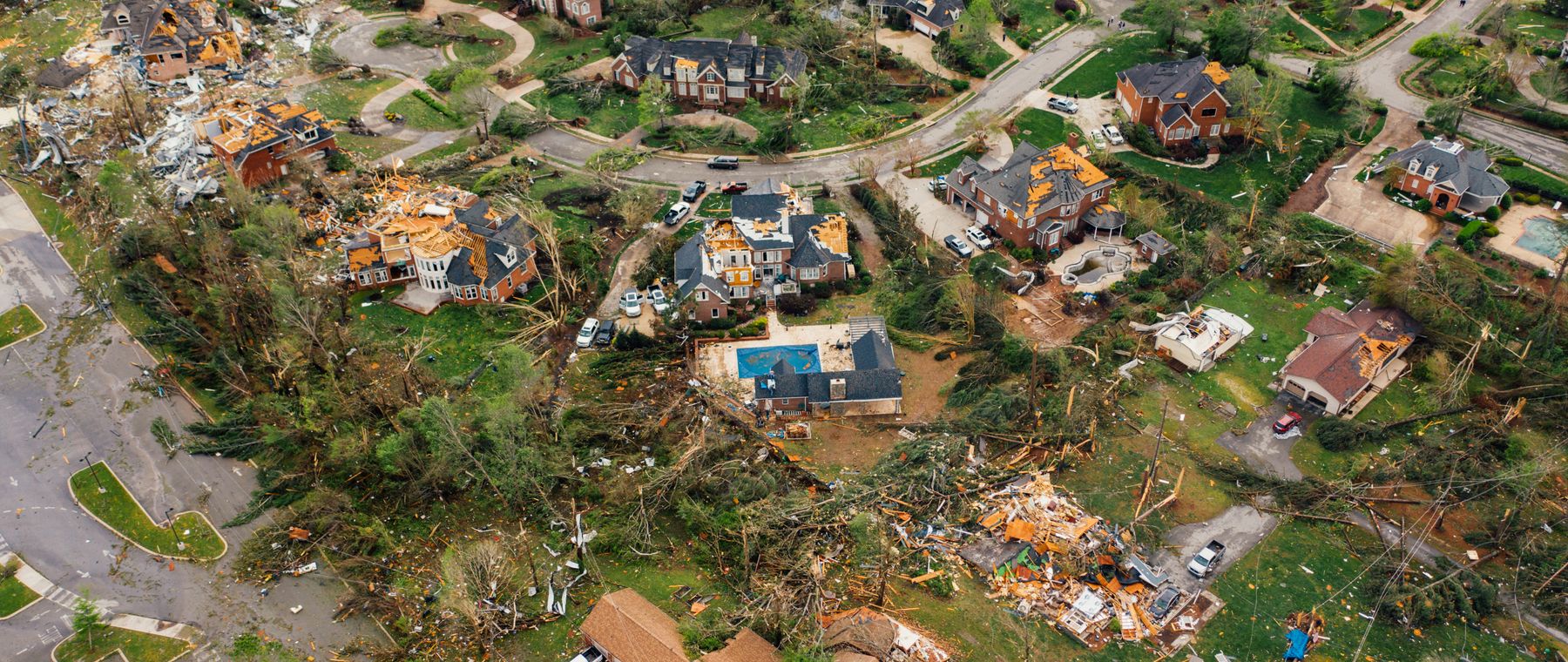 Aerial view of houses with damaged roofs and uprooted trees after a storm