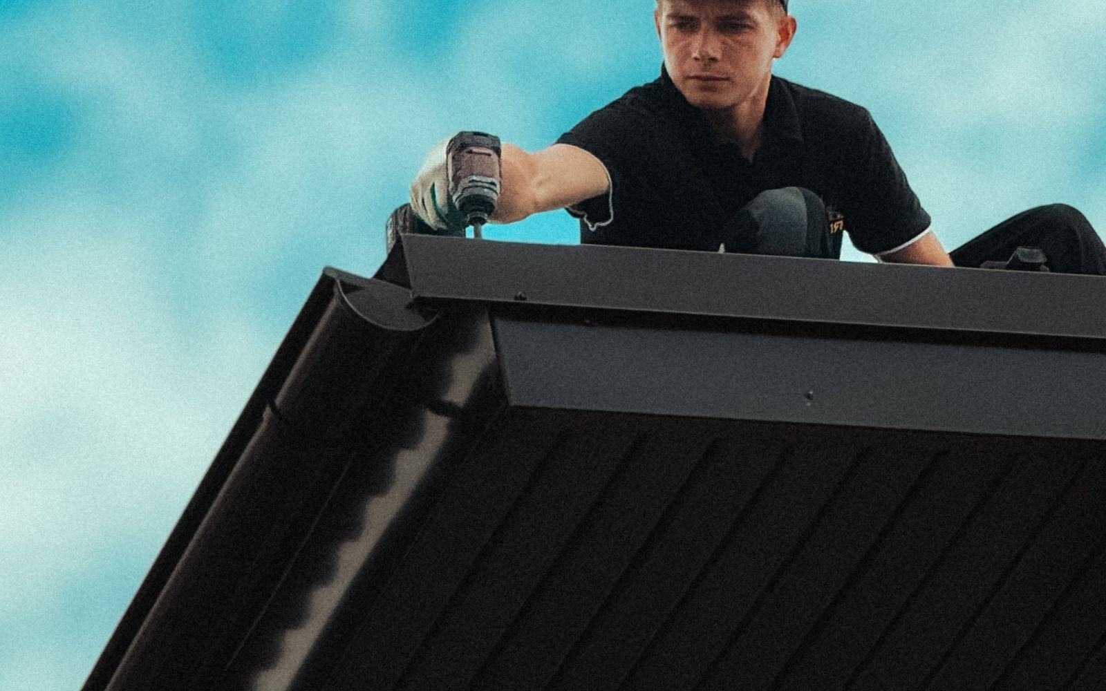 Roofer fastening along the edge of a dark metal roof