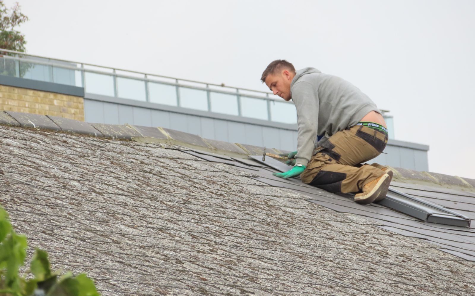 Roofer kneeling on a roof slope fitting a metal strip