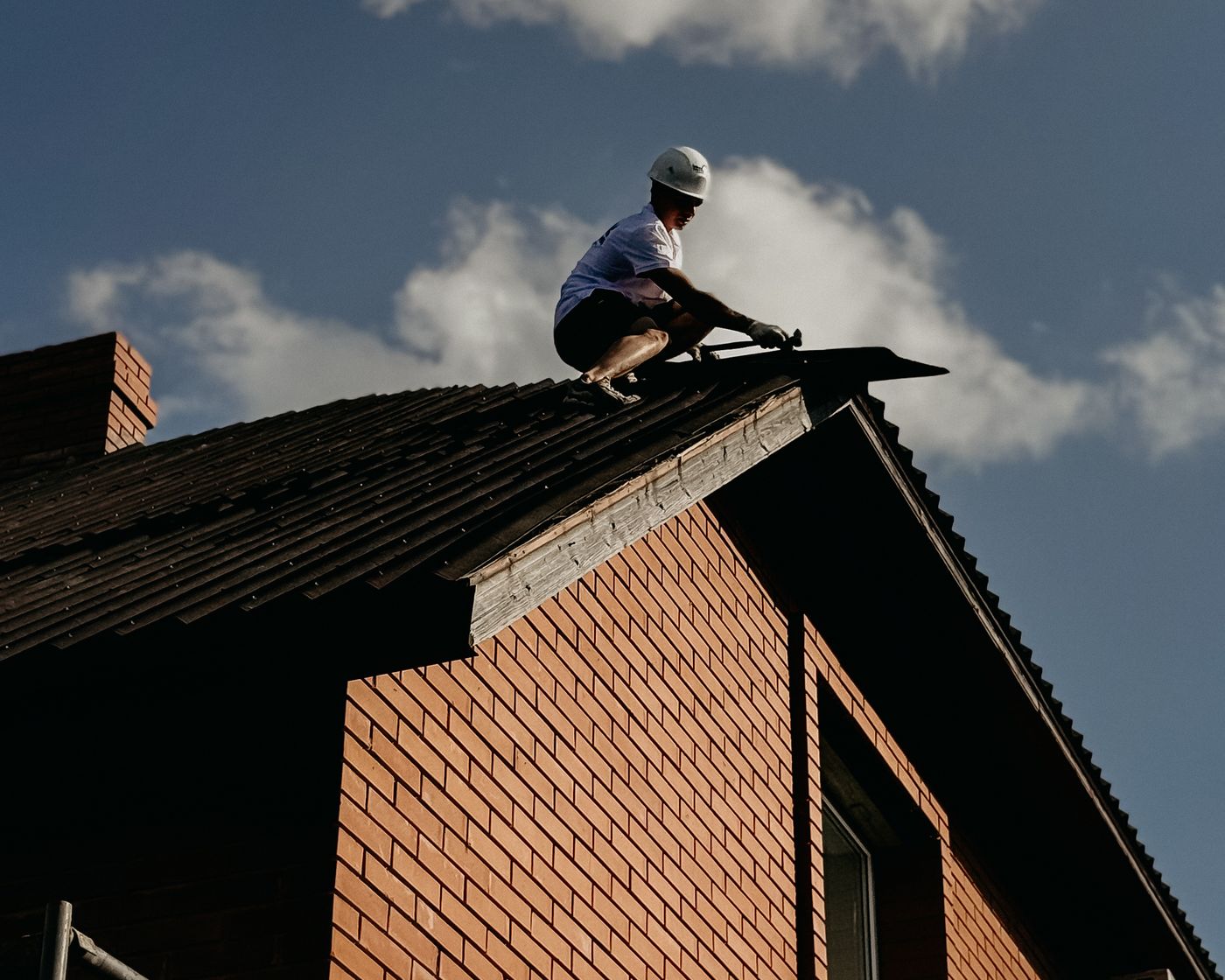 Roofer working on the ridge of a dark roof above a brick gable