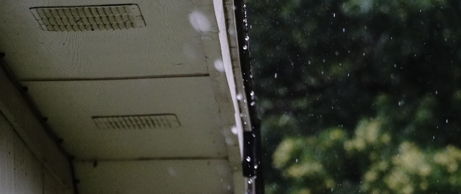 Vented soffit panel over a gutter, with rain falling