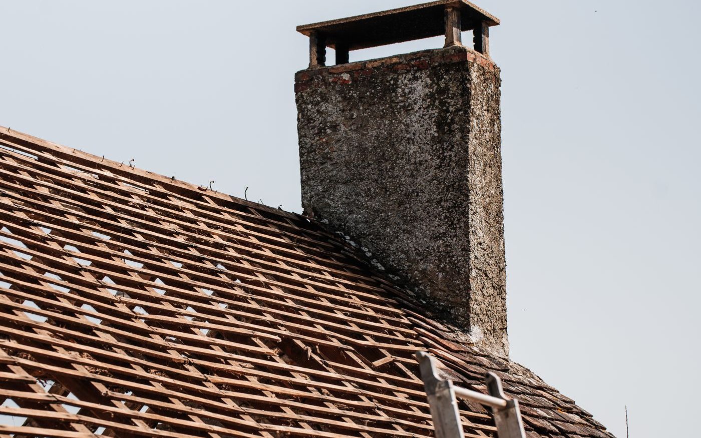 Old roof stripped back to battens beside a stone chimney