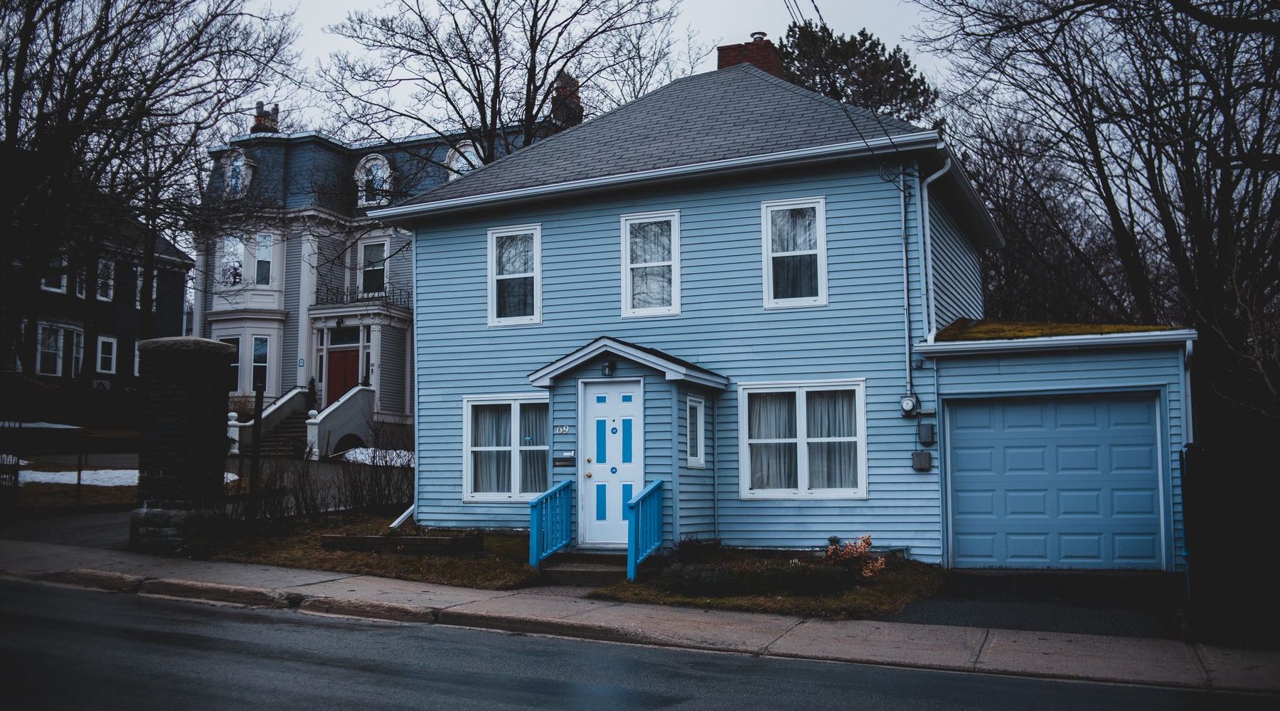 Light blue clapboard house with a white door and a garage