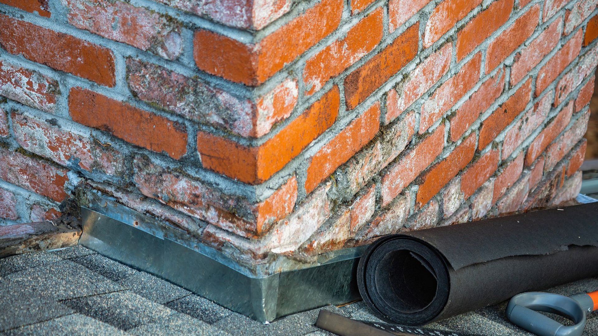 Brick base with metal flashing and a roll of membrane beside it