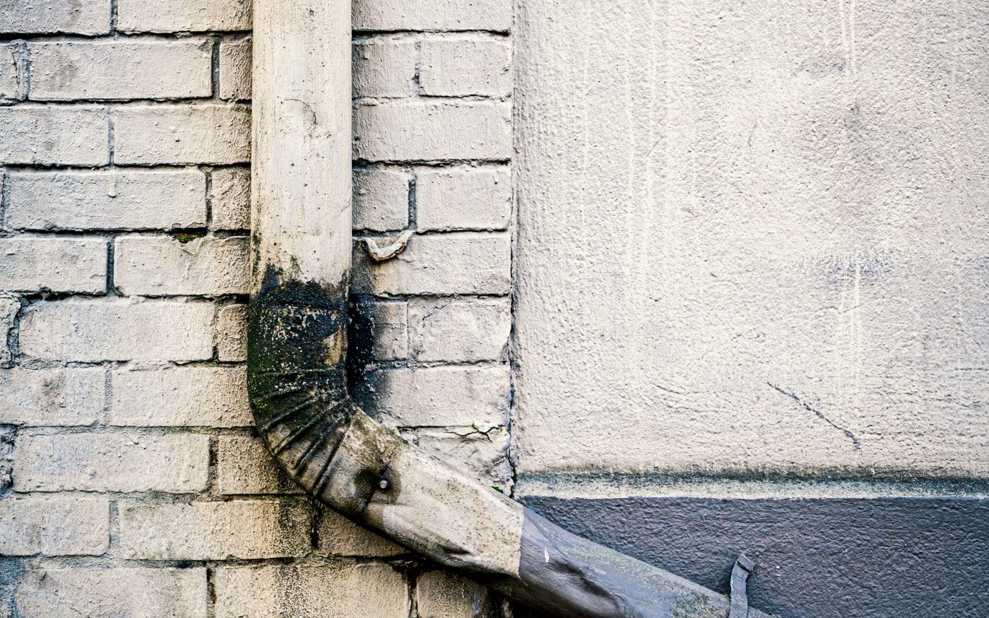 Downspout on a brick wall with weeds growing from a crack