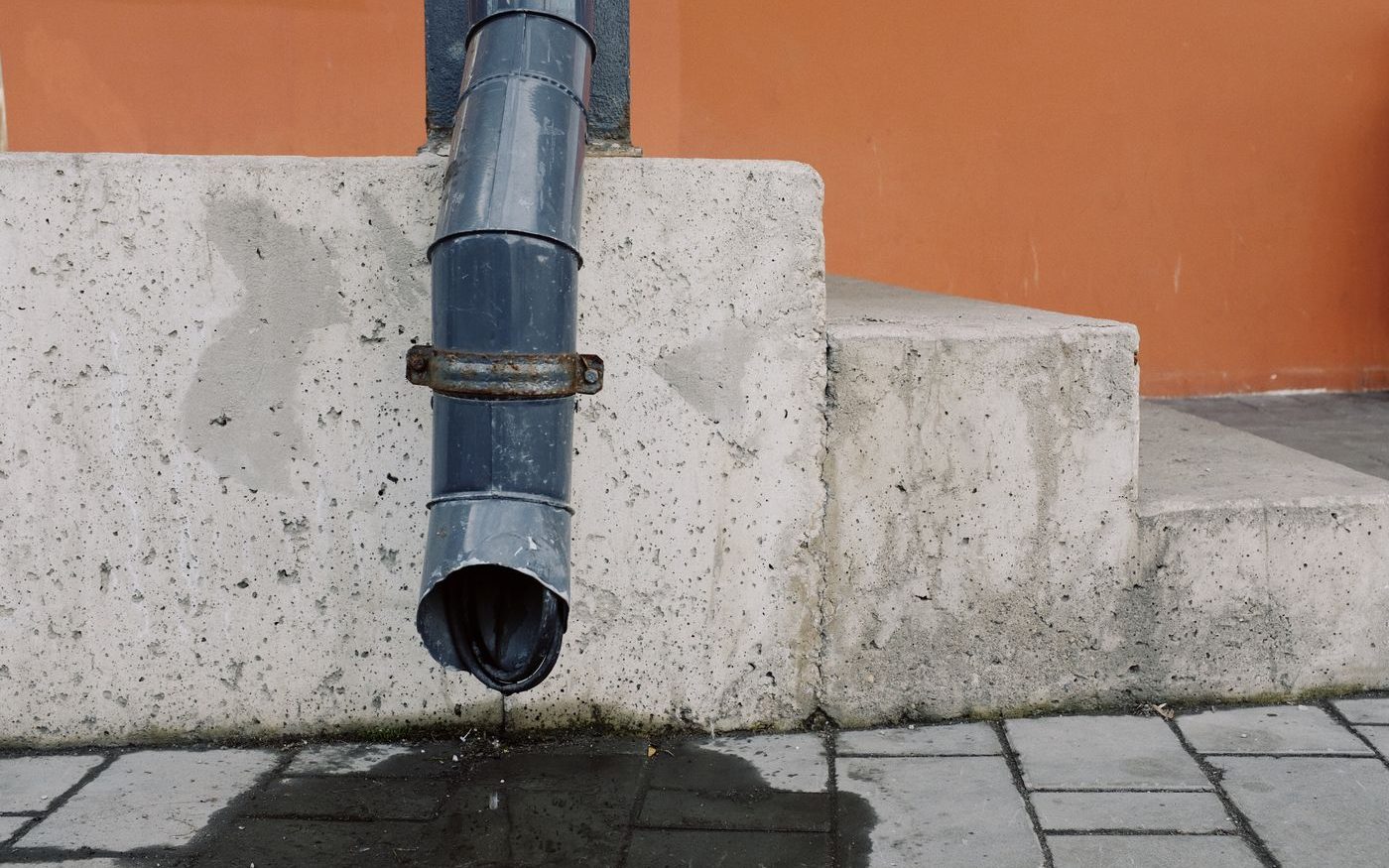 Downspout ending against a concrete step, water dripping from it