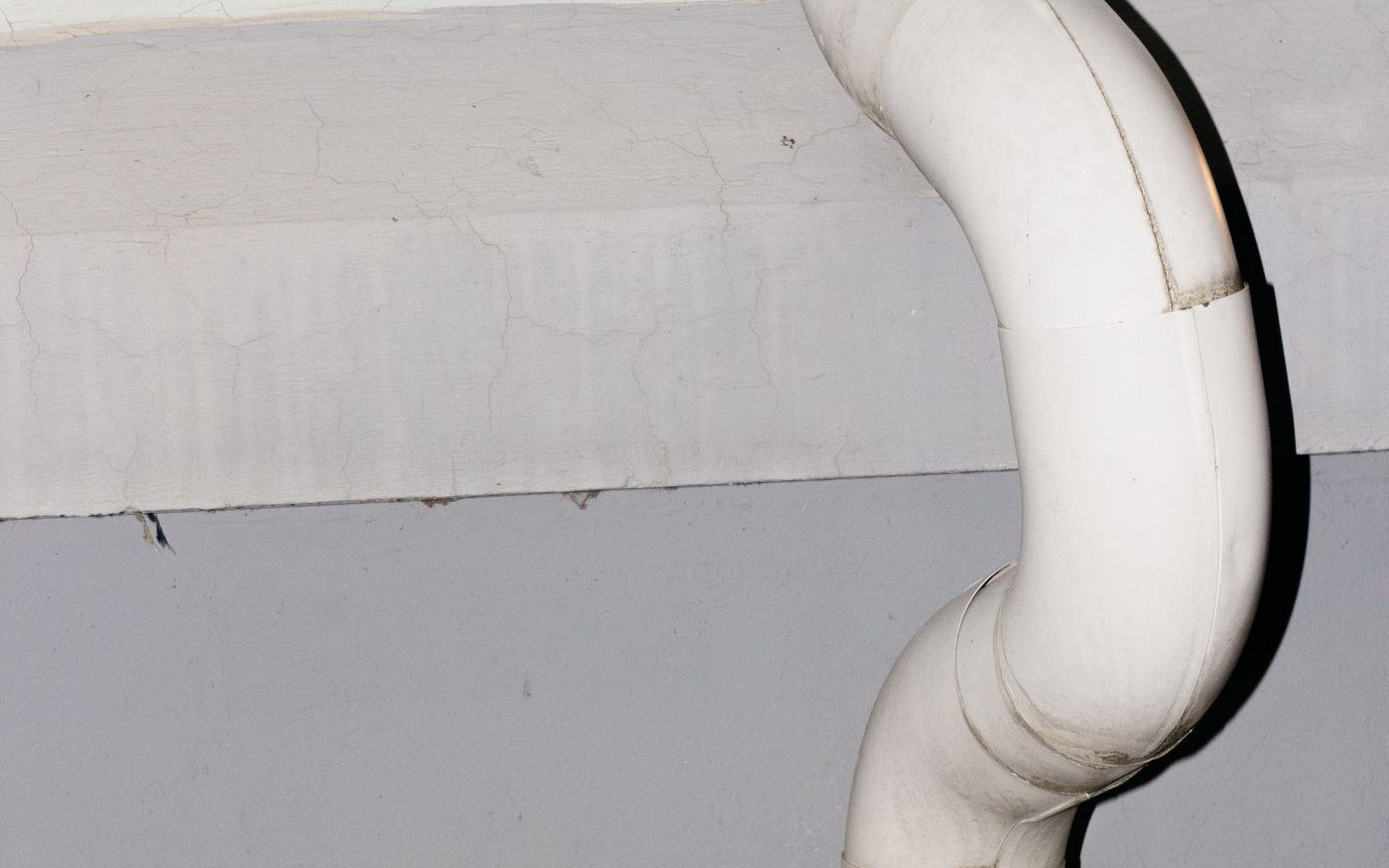 Curved white downspout against a gray wall