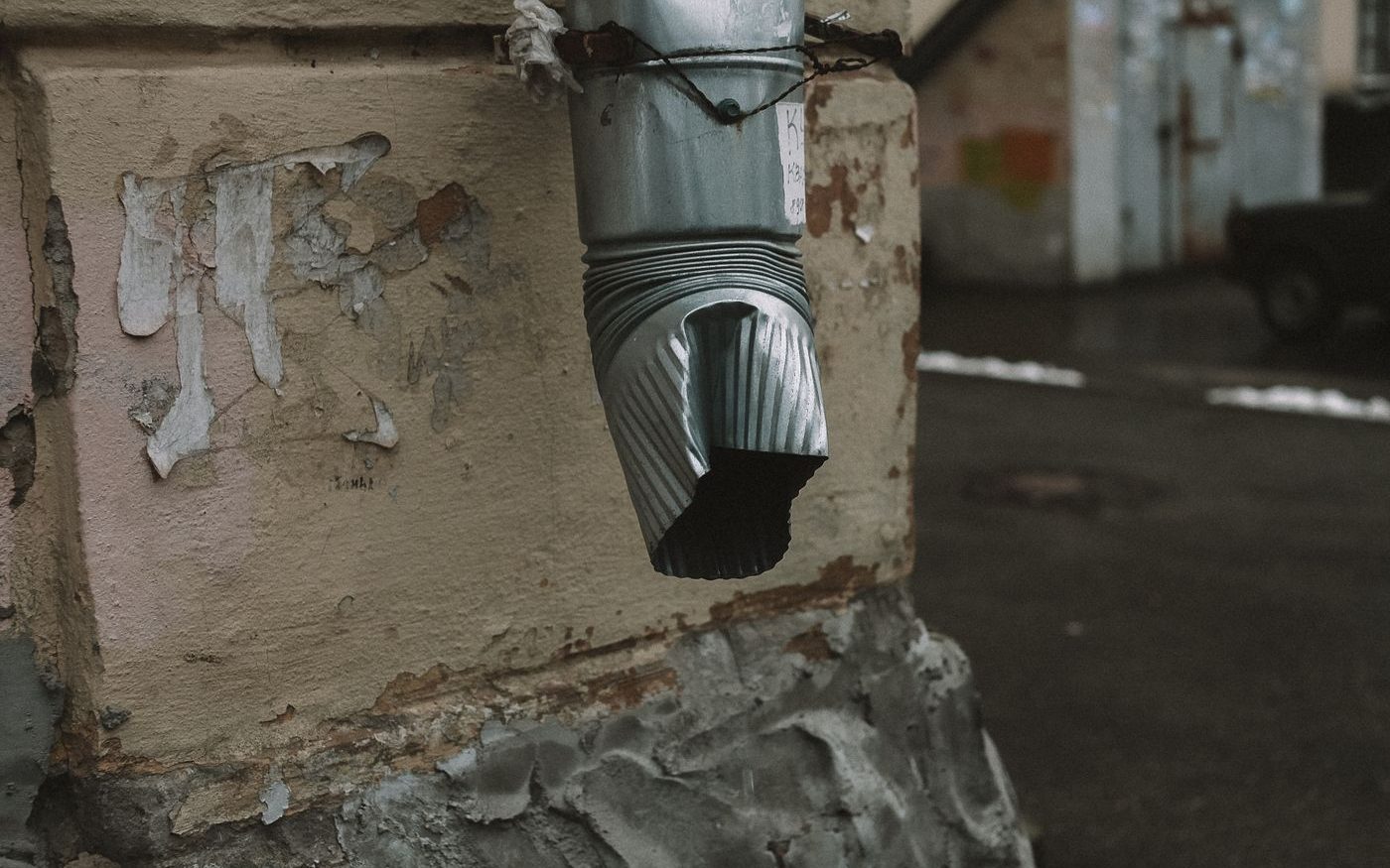Downspout outlet over a crumbling wall base with peeling paint