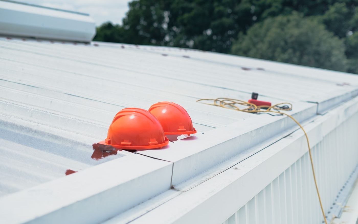 Two red hard hats resting on a white metal roof