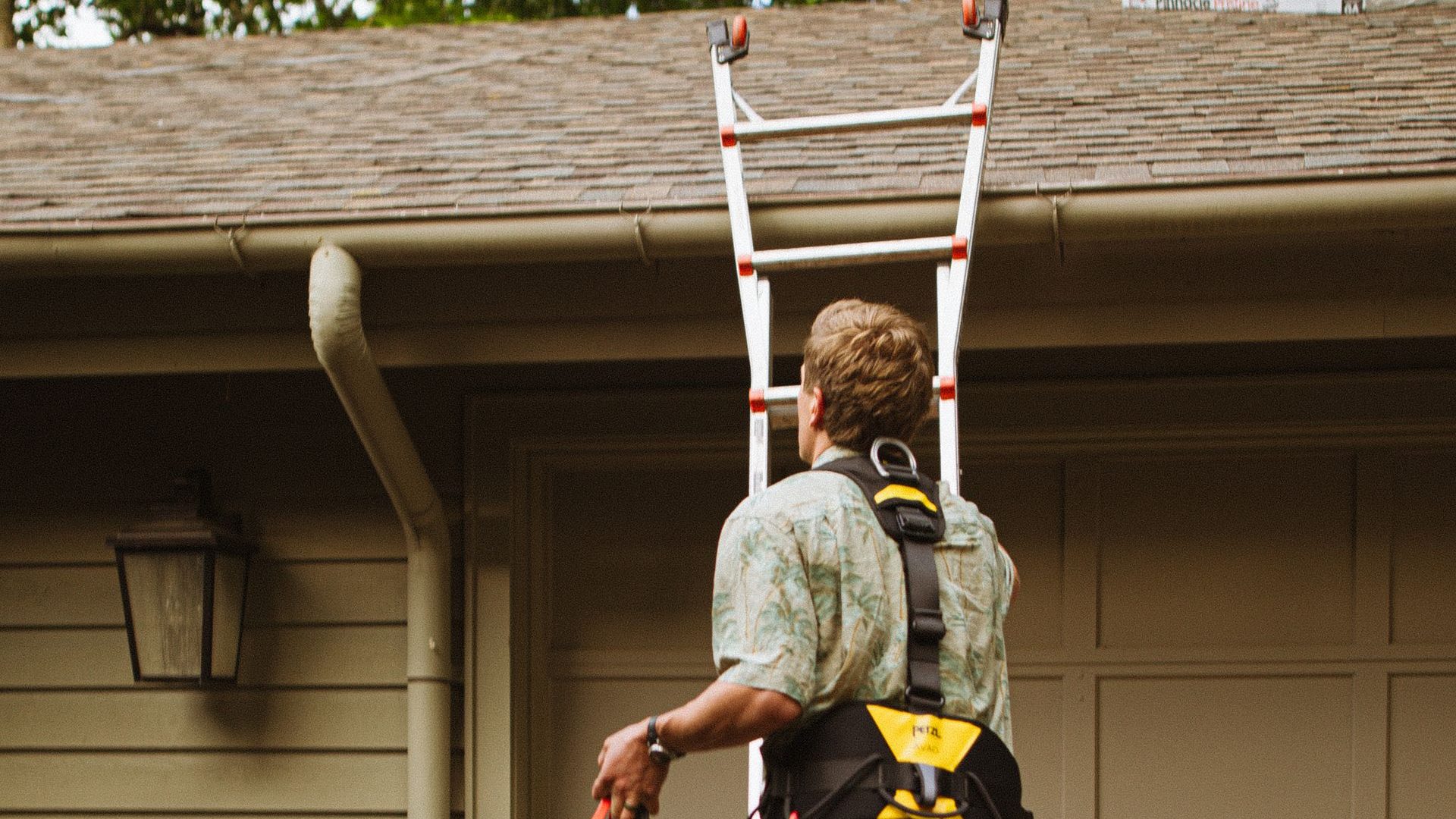 Roofer in a harness climbing a ladder to a shingle roof edge