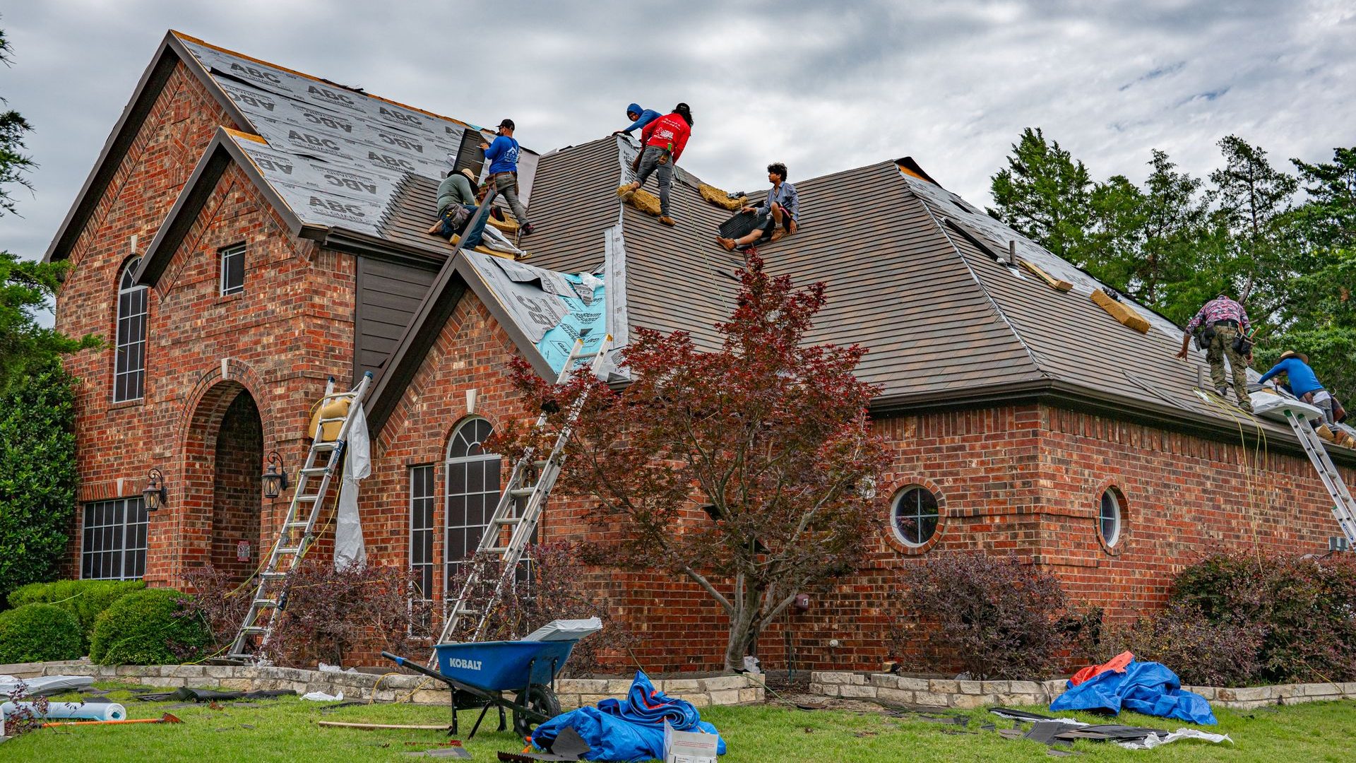 Crew working across the roof of a brick house, ladders at the eaves