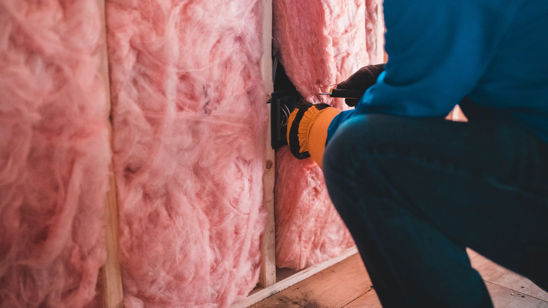Worker fitting pink insulation between wall studs