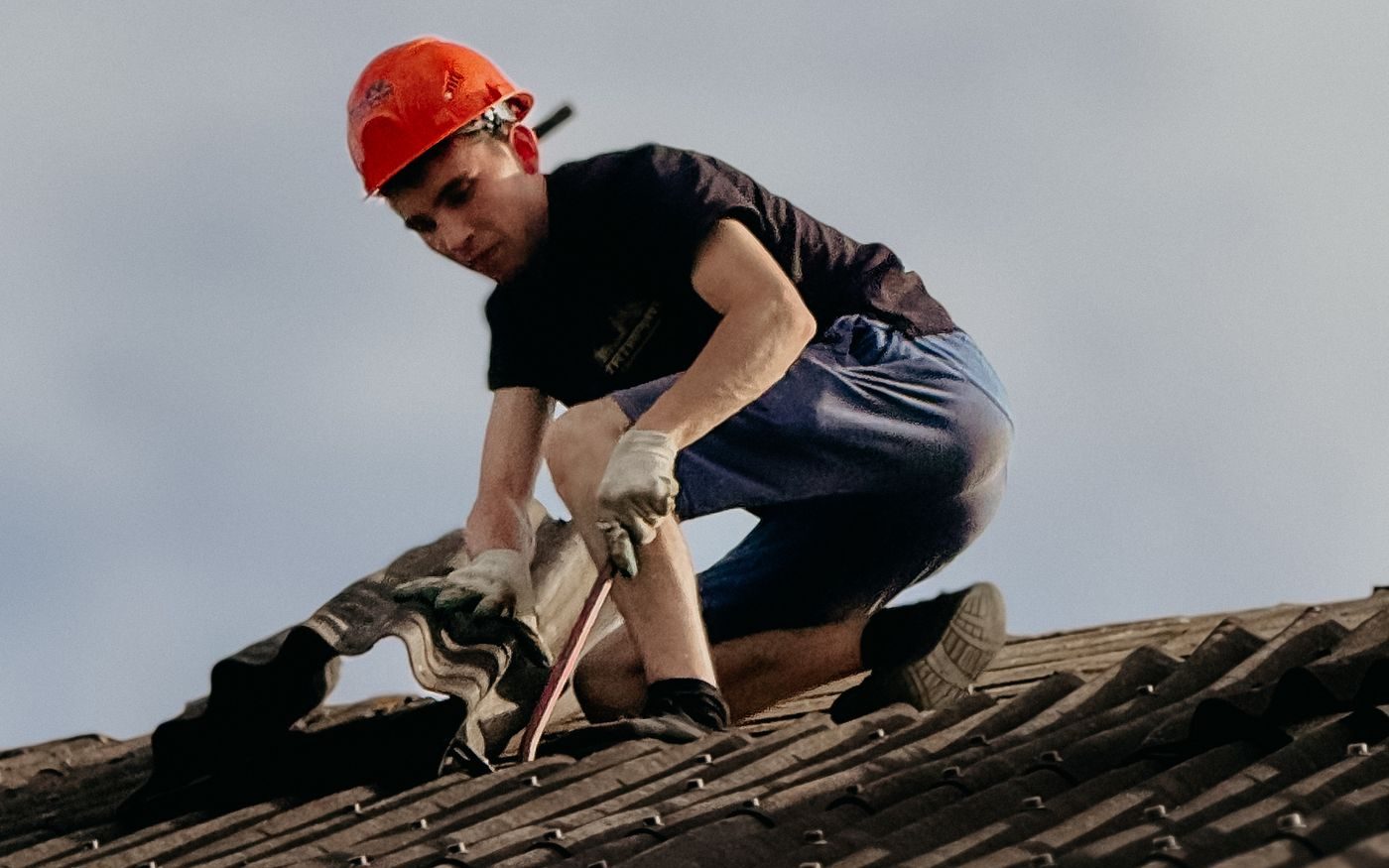 Roofer in a hard hat lifting a damaged section of roofing by hand
