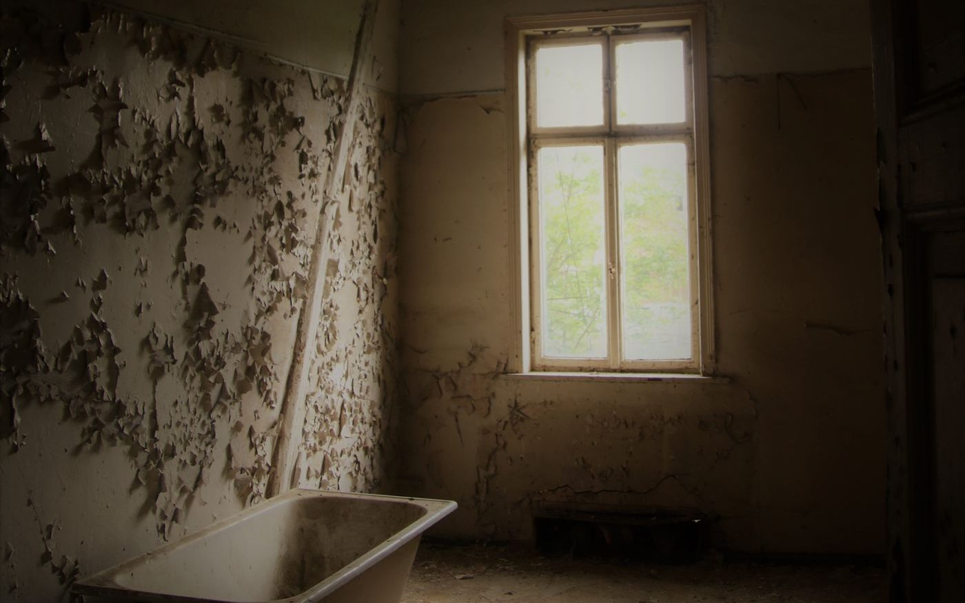 Paint peeling in flakes off an interior wall beside a window