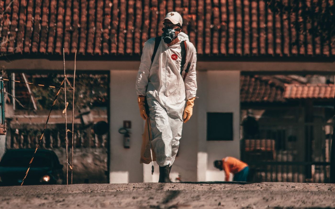 Person in a full protective suit and respirator walking outside a house