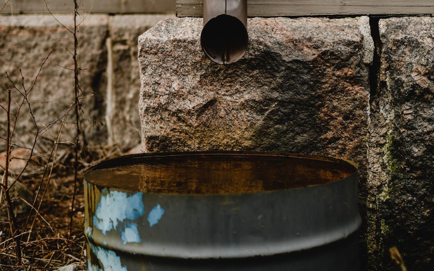 Downspout emptying into a metal barrel beside a wooden wall