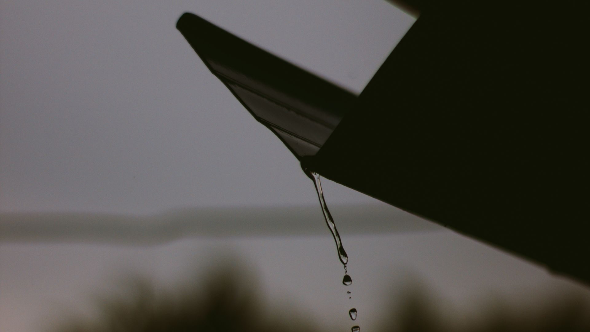 Water dripping off a roof edge against a dark sky