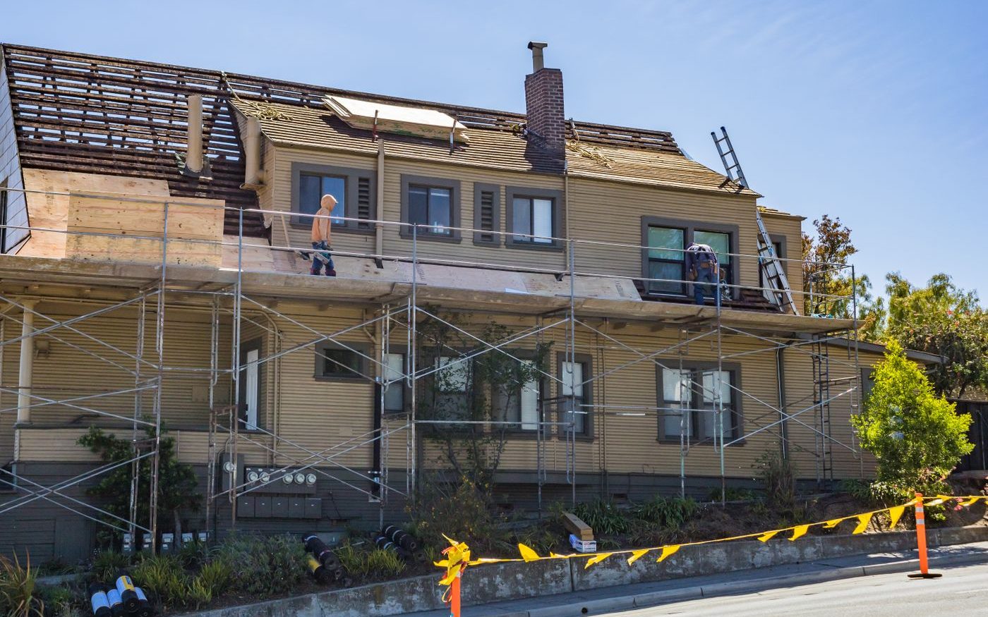 Two story house wrapped in scaffolding with workers on the roof