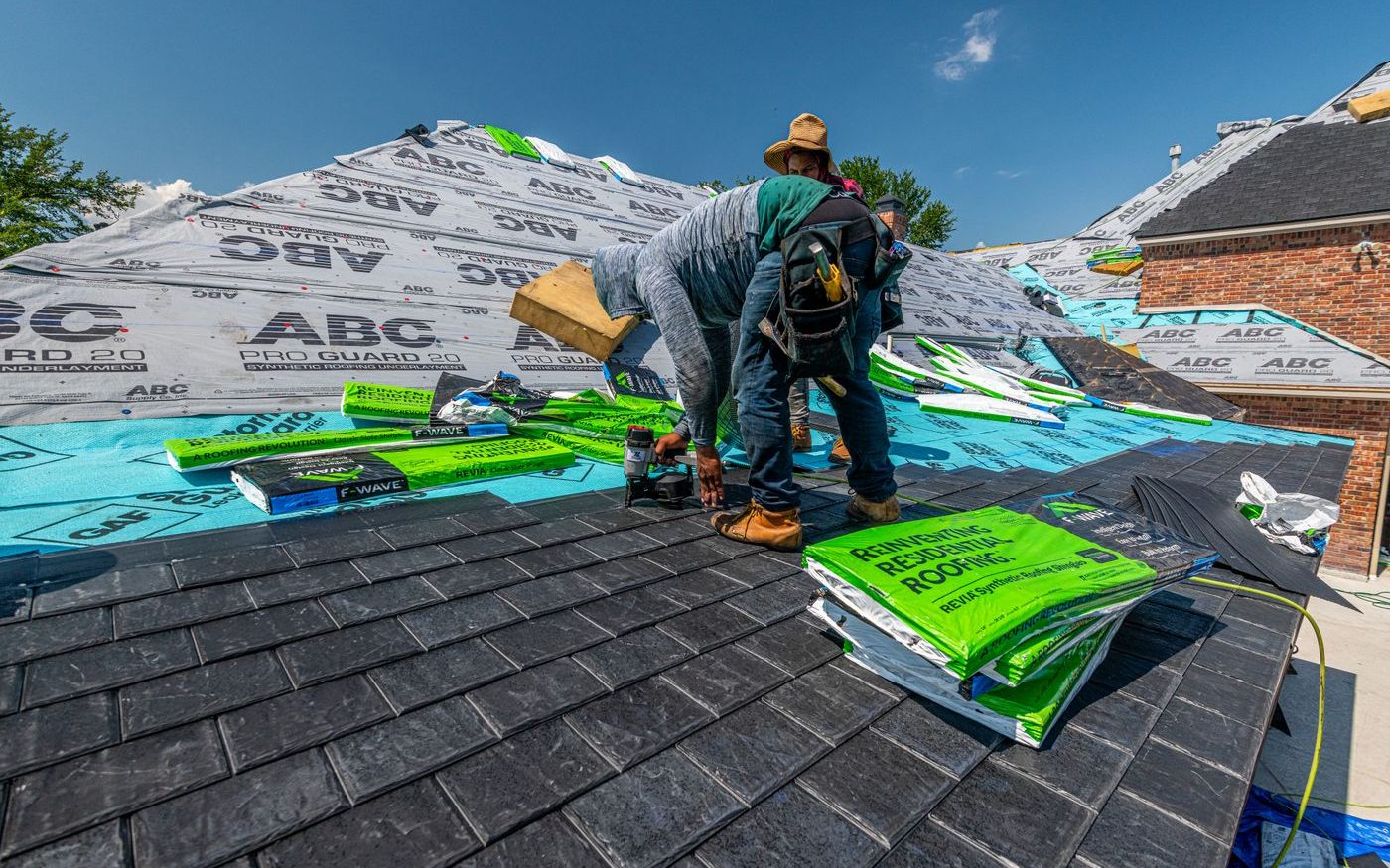 Roofers laying synthetic slate over underlayment on a brick house