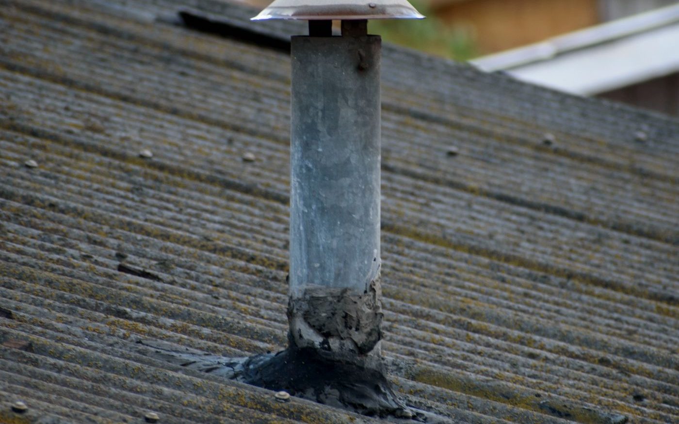 Vent pipe through a corrugated roof, its seal cracked at the base