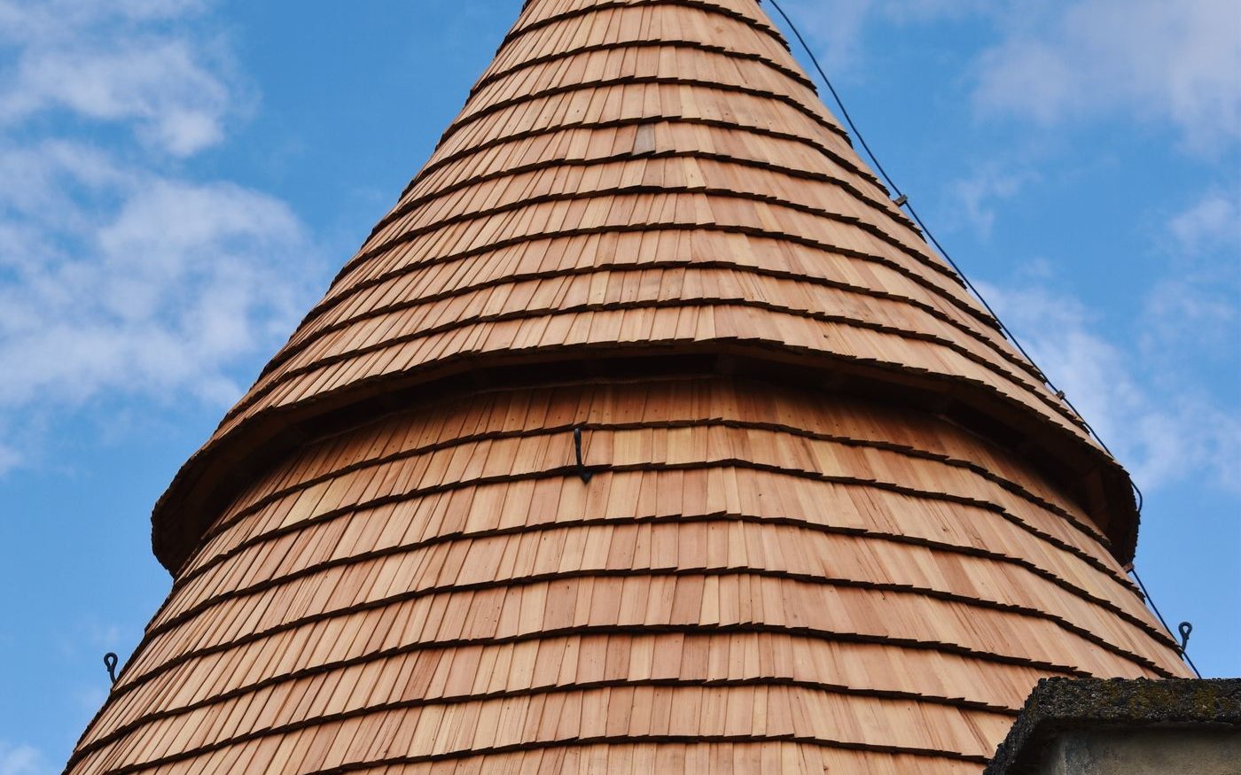 Conical tower roof clad in wooden shakes against a blue sky