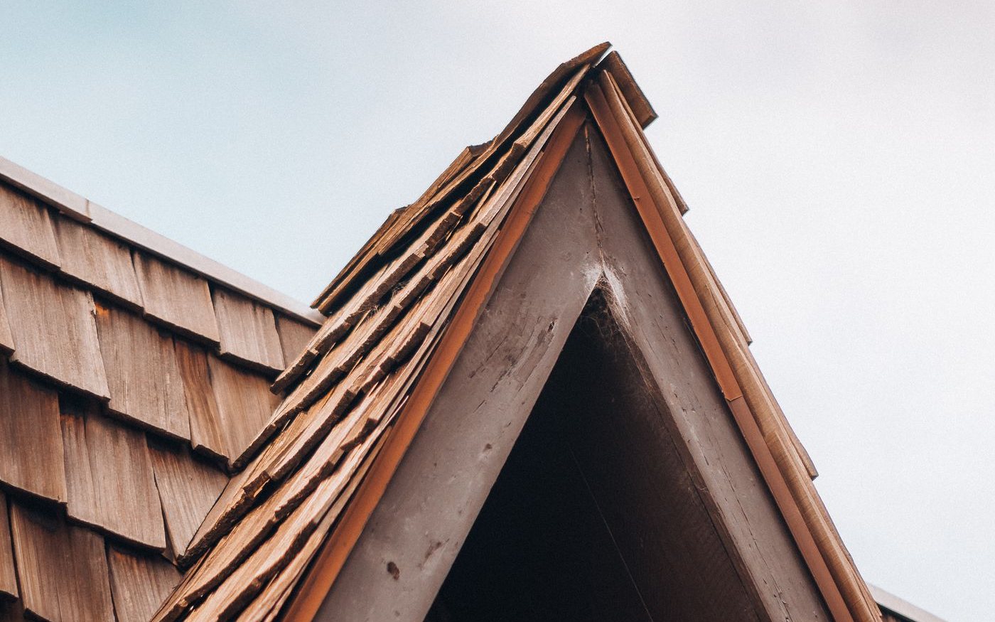 Gable end of a roof covered in wooden shakes against a pale sky