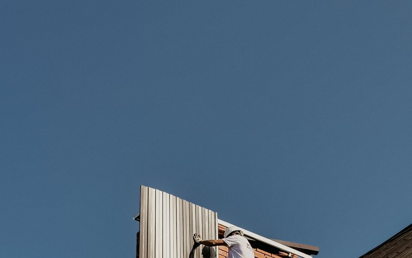 Workers fitting metal roof panels on a steep roof