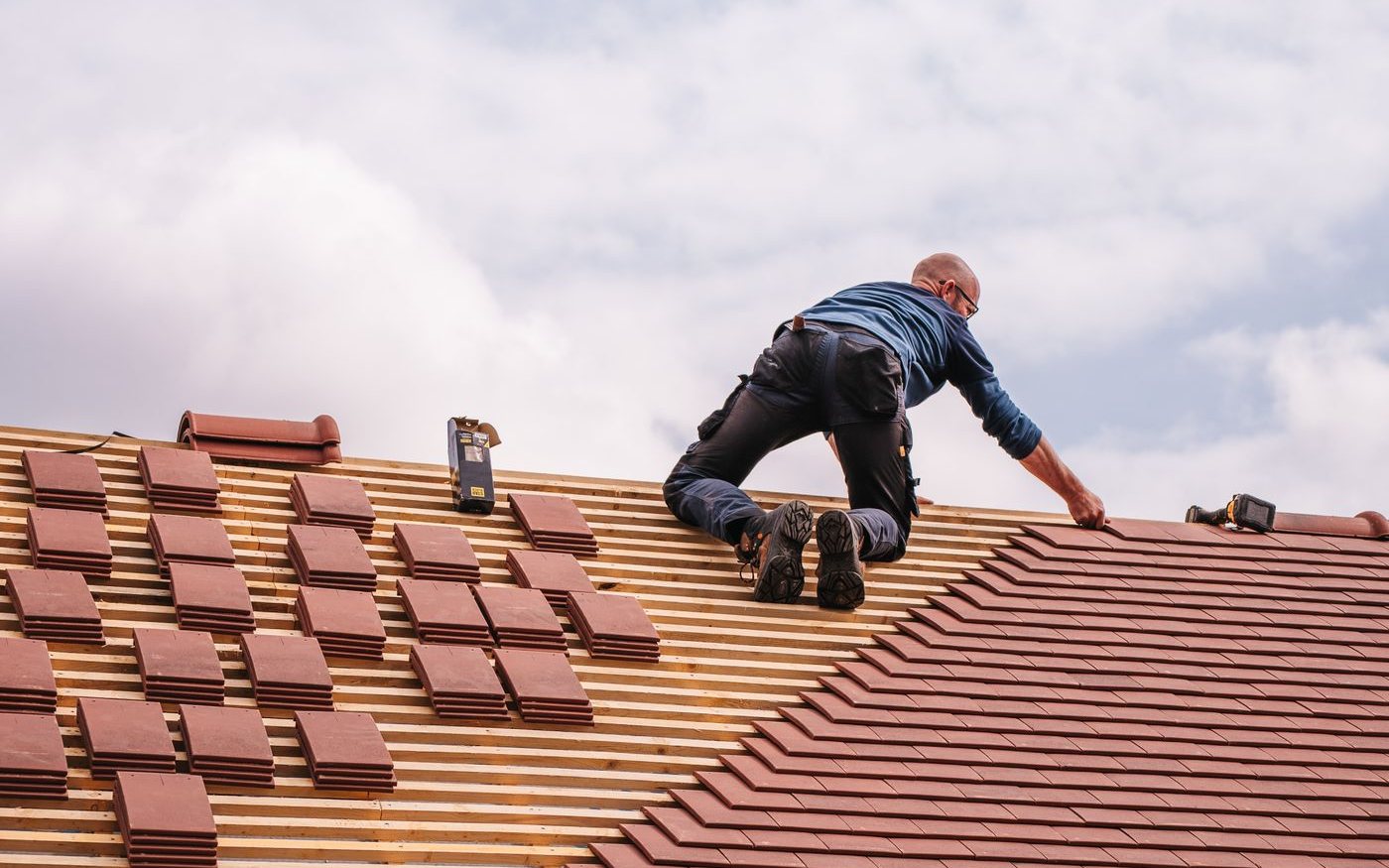 Roofer laying clay tiles near the ridge of a roof