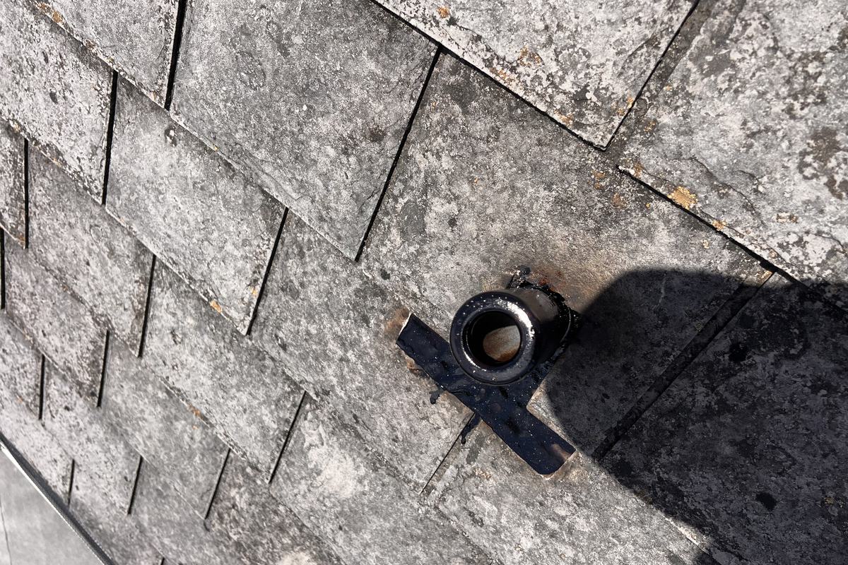 Weathered asphalt shingles around a cracked pipe boot
