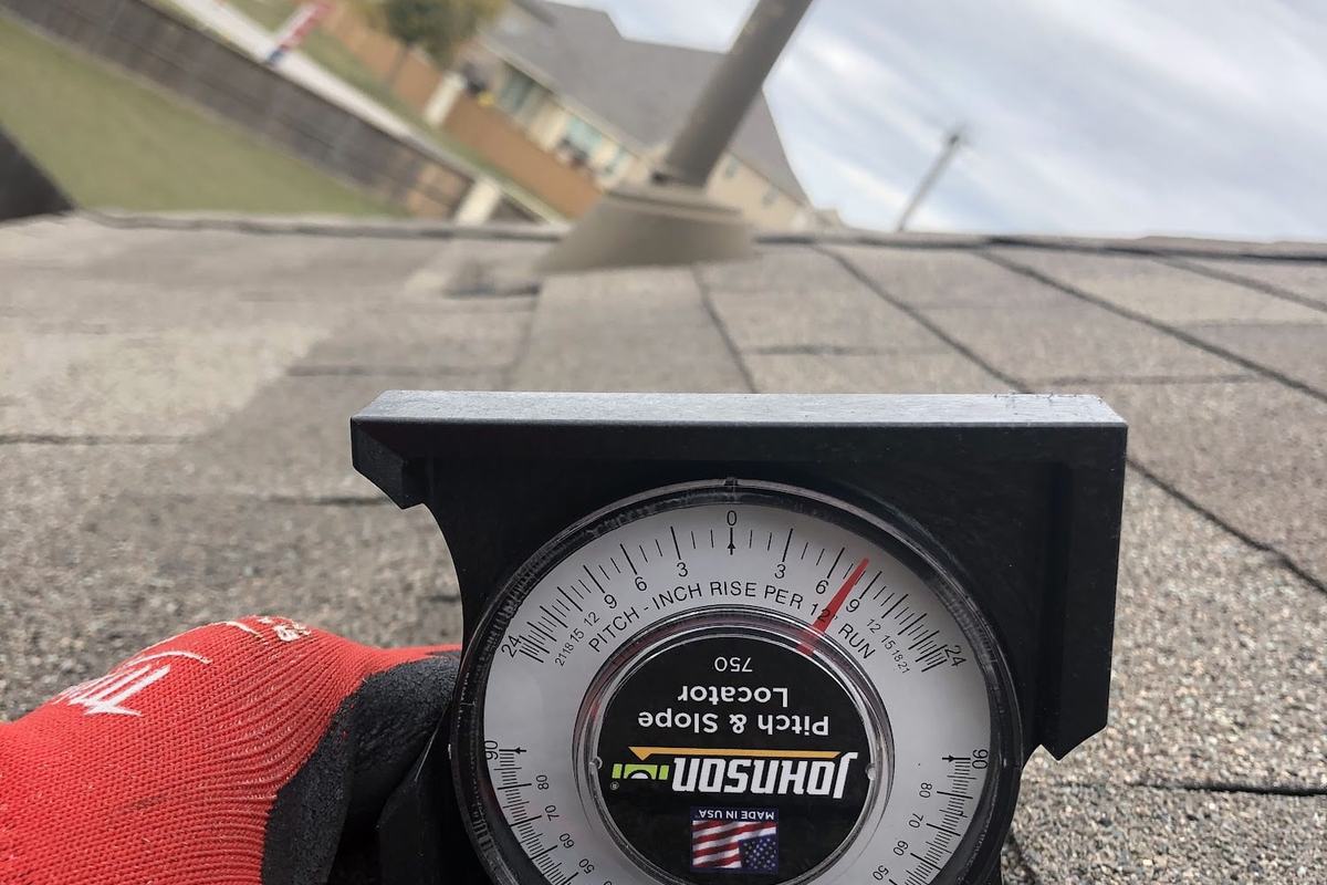 Gloved hand holding a pitch gauge on a shingle roof