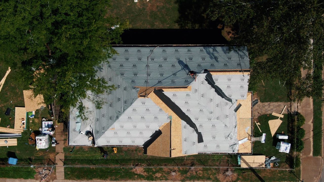 Overhead view of a house mid re-roof, new underlayment going down over bare decking