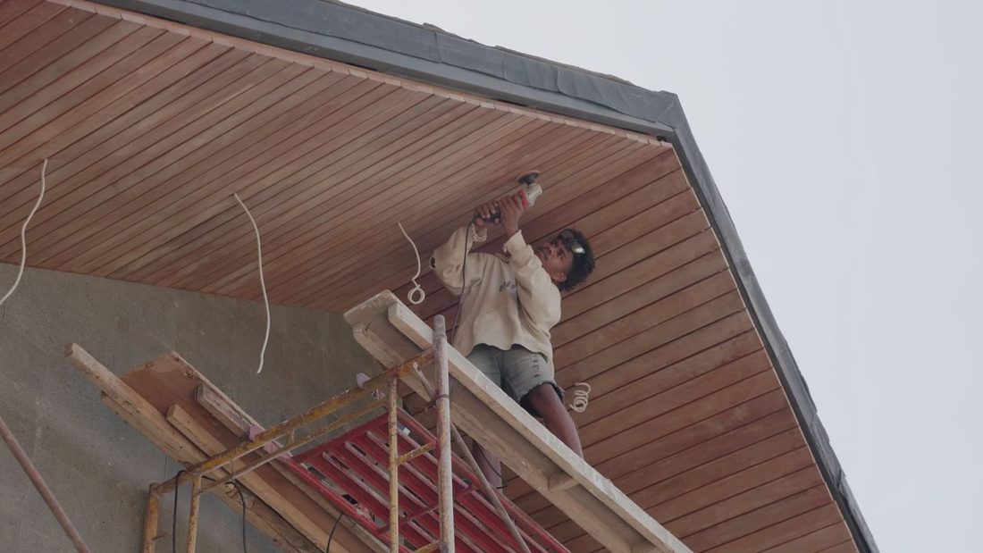 Worker fixing new wood soffit boards to the underside of an overhang from a scaffold